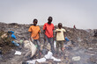 Group of poor African boys looking for recyclable items standing together amid burning garbage in an illegal landfill; informal waste management in developing countries