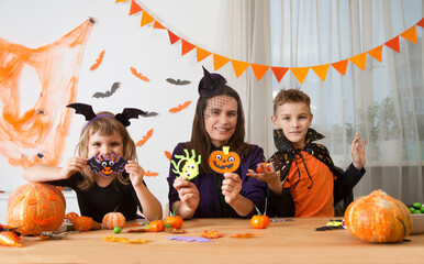 mom with two children in masquerade costumes make decor and crafts for the halloween holiday
