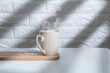 Cup of hot drink with smoke. White cup with coffee on white table in sunlight.