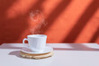 Cup of hot coffee. White cup and saucer on white table in sunlight.
