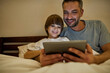 © Svitlana - Smiling father and son watch digital tablet in bed