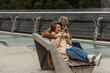 © LIGHTFIELD STUDIOS - happy senior man hugging positive wife while sitting on bench near bridge guard rail.