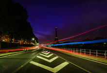 Road markings and coloured light trails at night on a straight road in Paris.