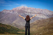 © ЮРИЙ ПОЗДНИКОВ - A young woman stands on top of a mountain with her arms outstretched.