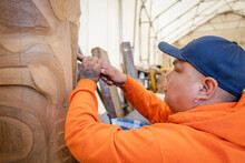 Male Indigenous Artist Carving Wood Totem Pole In Workshop