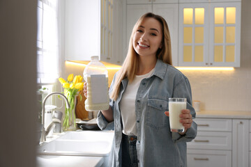 Canvas Print - Young woman with gallon bottle of milk and glass near white countertop in kitchen