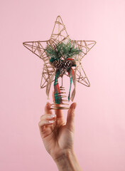 Wall Mural - Woman's hand holds craft homemade Christmas tree top star on a pink background