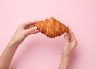 Female hands holding a croissant on a pink background