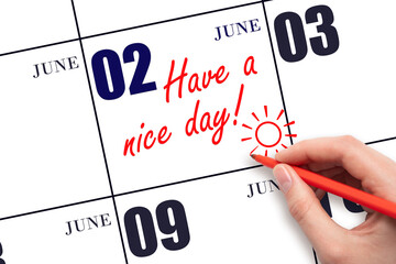 The hand writing the text Have a nice day and drawing the sun on the calendar date June 2