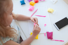The Girl Cuts And Sculpts From Plasticine, Is Engaged In Creativity At A White Table Against A White Wall, Early Childhood Development, Kindergarten