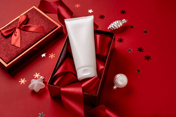 White bottle cosmetic product in red giftbox and on red background. Christmas sale of beauty products concept. Top view with place for text.