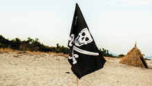 Black Pirate Flag With Skull Symbol On The Desert Island