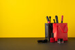 Black friday shopping concept. Photo of red and black paper bags with cosmetics brushes lip gloss liner eyebrow gel and nail polish on desktop yellow wall background with copyspace