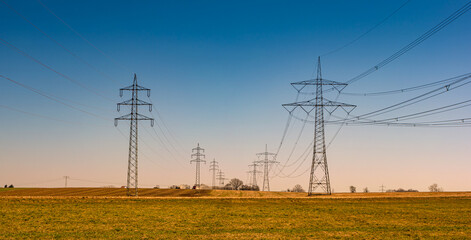 Wall Mural - Beautiful farm landscape and high voltage power lines pylons in Germany at Autumn colors during sunset with blue sky. Concept of energy supply and energy crisis.