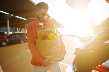 Wall Mural - Young man with shopping bag near the car. Consumerism, sale, purchases, shopping, Healthy food,  lifestyle concept.