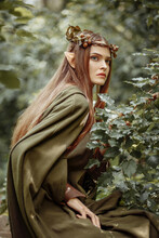 Elf Girl Dressed In A Cape And With A Wreath On Her Head In The Forest. Fantasy Elf From The Forest. Beautiful Fantasy Woman.