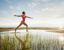 Girl (12-13) In Swimsuit Jumping Above Lake At Sunrise