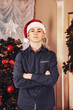 Portrait teen caucasian boy with santa hat in living room with mirror and christmas tree at cozy home, looking at camera. Family atmospheric moment Merry Christmas, Happy New Year. Copy text space
