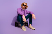 Full Body Photo Of Cool Beard Red Hairdo Guy Sit Listen Boombox Wear Sunglass Hoodie Jeans Shoes Isolated On Purple Background