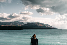 Caucasian Boy With Long Loose Disheveled Hair Standing Calm Looking At The Sea And Mountains Wearing A Black T-shirt Under A Gray Sky And Storm Clouds, Mount Cook, New Zealand