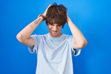 Sticker - Hispanic young man standing over blue background suffering from headache desperate and stressed because pain and migraine. hands on head.