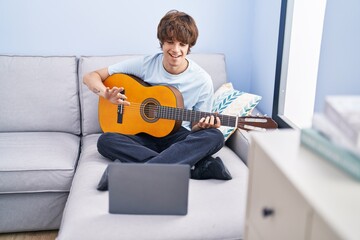 Poster - Young blond man having online classical guitar class sitting on sofa at home