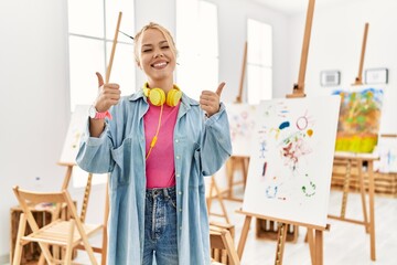 Poster - Young caucasian girl at art studio success sign doing positive gesture with hand, thumbs up smiling and happy. cheerful expression and winner gesture.