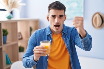 Sticker - Handsome hispanic man drinking glass of orange juice annoyed and frustrated shouting with anger, yelling crazy with anger and hand raised