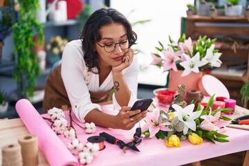 Sticker - Young beautiful hispanic woman florist using smartphone leaning on table at flower shop