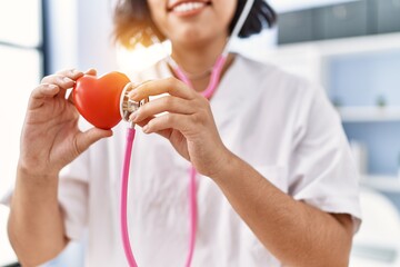 Wall Mural - Young latin woman wearing doctor uniform auscultating heart at clinic