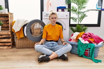 Sticker - Young blonde woman doing laundry sitting by washing machine skeptic and nervous, frowning upset because of problem. negative person.