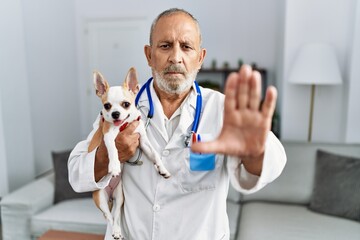 Wall Mural - Mature veterinarian man checking dog health with open hand doing stop sign with serious and confident expression, defense gesture