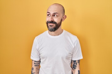 Canvas Print - Young hispanic man with tattoos standing over yellow background smiling looking to the side and staring away thinking.