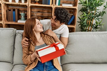 Sticker - Young couple smiling happy sitting on the sofa surprise with anniversary gift at home.