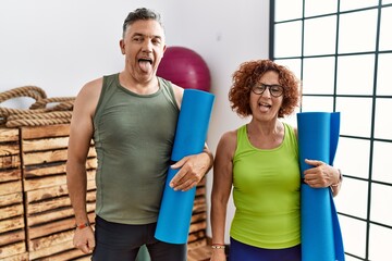 Poster - Middle age couple holding yoga mat sticking tongue out happy with funny expression. emotion concept.