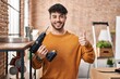 © Krakenimages.com - Hispanic man with beard holding screwdriver at new home smiling happy and positive, thumb up doing excellent and approval sign