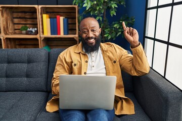 Poster - African american man using laptop at home sitting on the sofa surprised with an idea or question pointing finger with happy face, number one