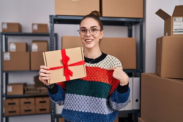 Canvas Print - Young hispanic girl working at small business ecommerce holding box pointing finger to one self smiling happy and proud