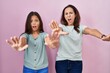 © Krakenimages.com - Young mother and daughter standing over pink background doing stop gesture with hands palms, angry and frustration expression