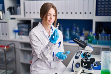 Poster - Young caucasian woman scientist smiling confident holding pill with tweezer at laboratory