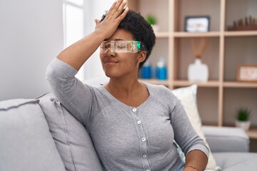 Wall Mural - Young african american woman wearing virtual reality glasses sitting on the sofa surprised with hand on head for mistake, remember error. forgot, bad memory concept.