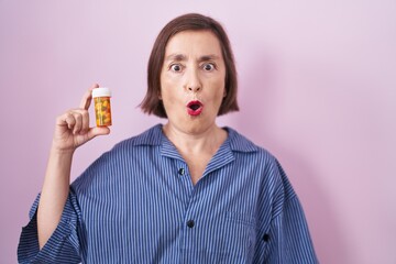 Sticker - Middle age hispanic woman holding pills scared and amazed with open mouth for surprise, disbelief face