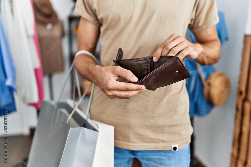 Young caucasian man holding empty wallet at clothing store