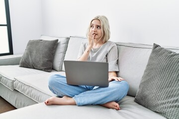 Poster - Young caucasian woman using laptop at home sitting on the sofa looking stressed and nervous with hands on mouth biting nails. anxiety problem.