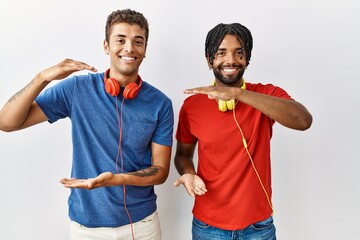 Poster - Young hispanic brothers standing over isolated background wearing headphones gesturing with hands showing big and large size sign, measure symbol. smiling looking at the camera. measuring concept.