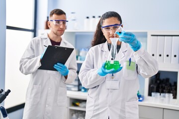 Wall Mural - Man and woman wearing scientist uniform write on document measuring liquid at laboratory