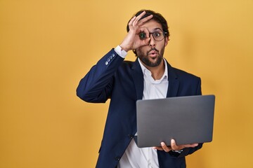 Poster - Handsome latin man working using computer laptop doing ok gesture shocked with surprised face, eye looking through fingers. unbelieving expression.