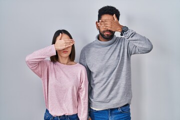 Sticker - Young hispanic couple standing together covering eyes with hand, looking serious and sad. sightless, hiding and rejection concept