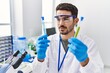 © Krakenimages.com - Young hispanic man wearing scientist uniform holding test tubes at laboratory