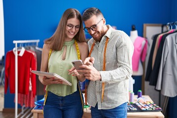 Man and woman tailors using smartphone holding notebook at clothing factory